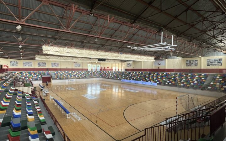 Interior del pabellón Esperanza Lag de Elche en septiembre de 2024, con pista polideportiva vacía y gradas de asientos multicolores.